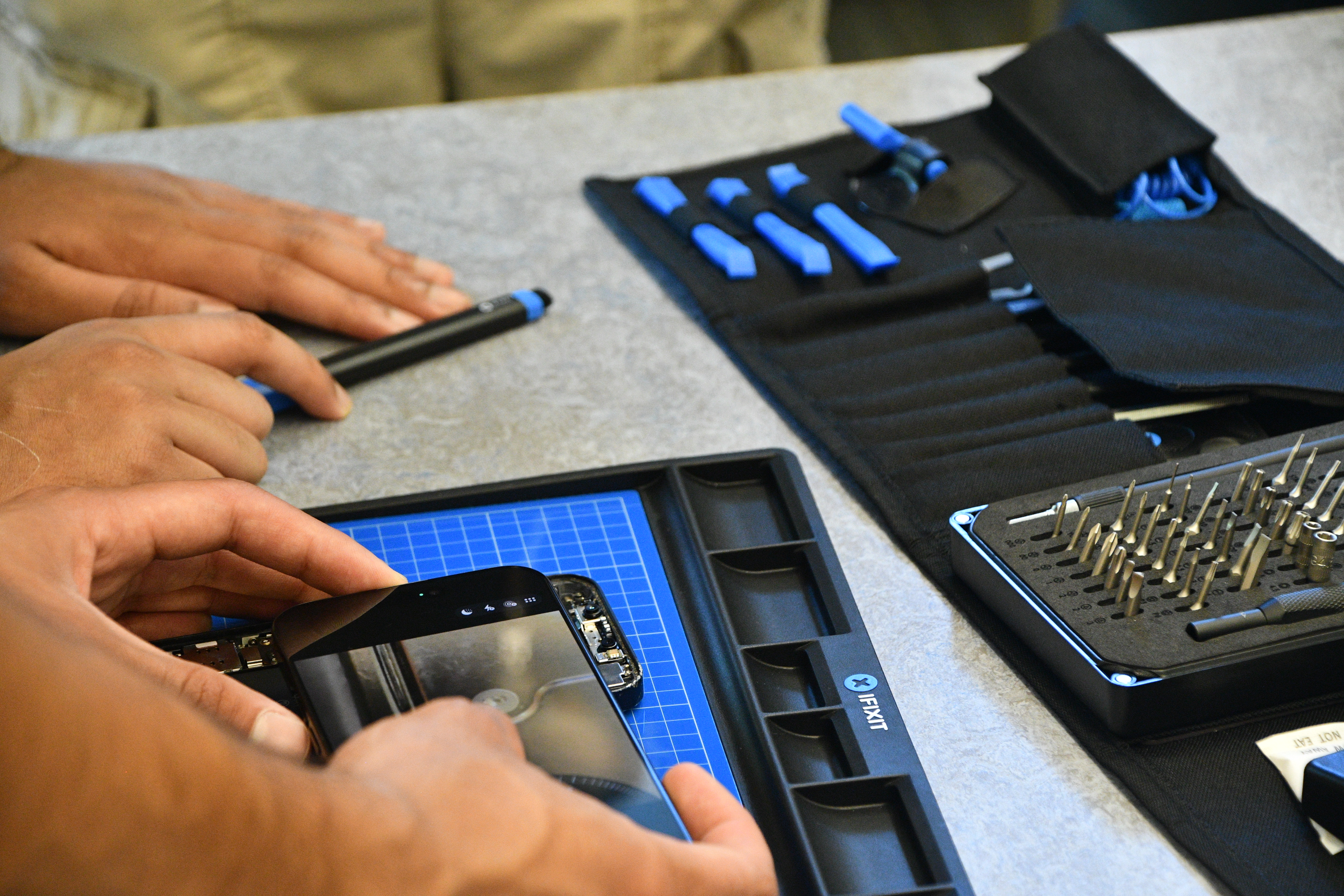 An iFixit Pro Tech Toolkit spread open beside a phone screen being removed