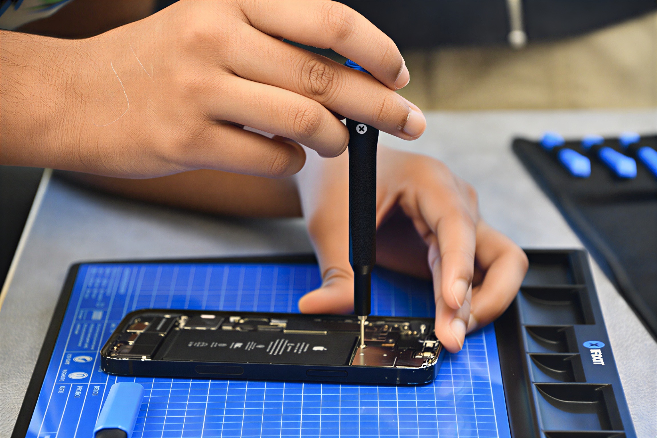 A student driving a screw out of an open iPhone on an iFixit mat