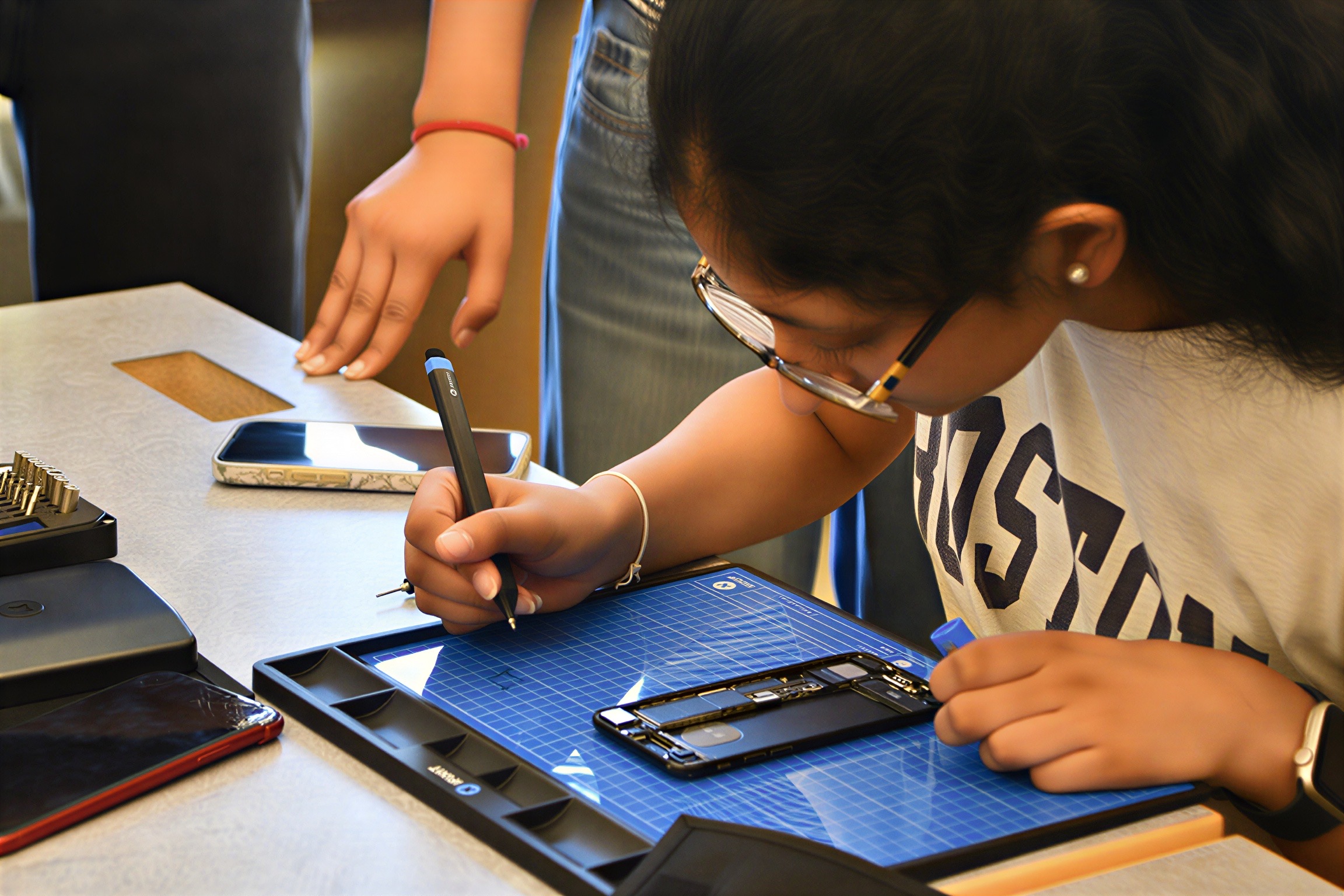 A student marking screw positions on an iFixit mat next to an opened phone