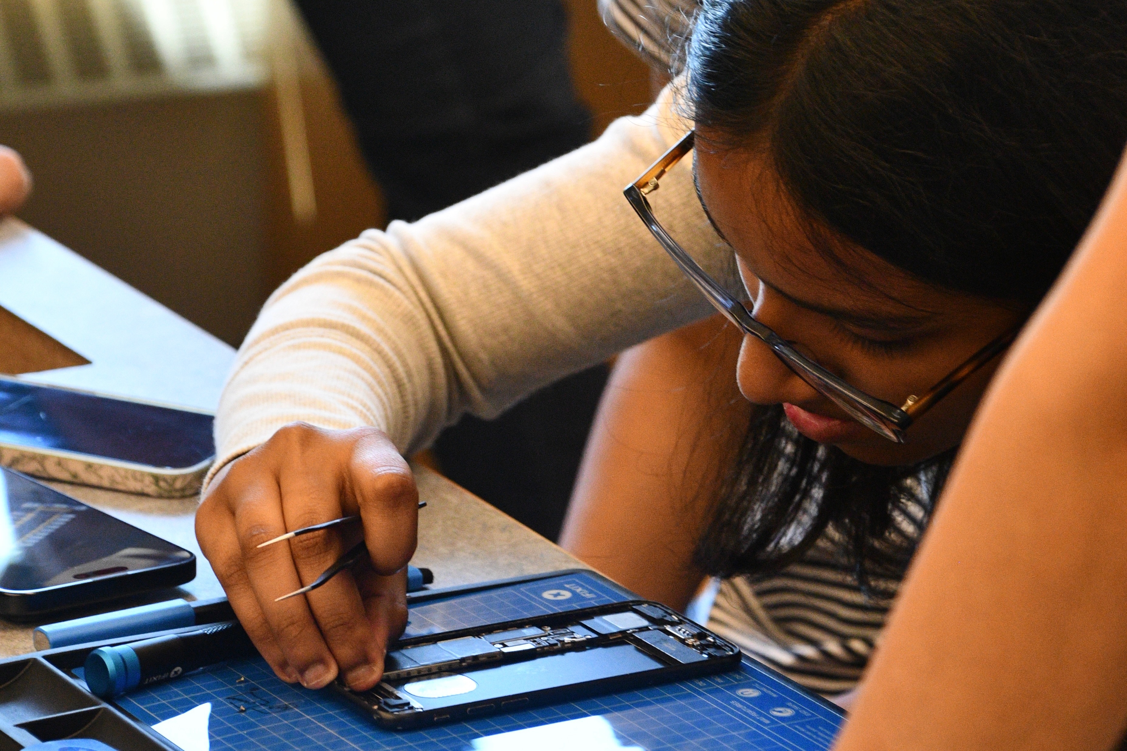 A student lifting a component out of an open phone with precision tweezers