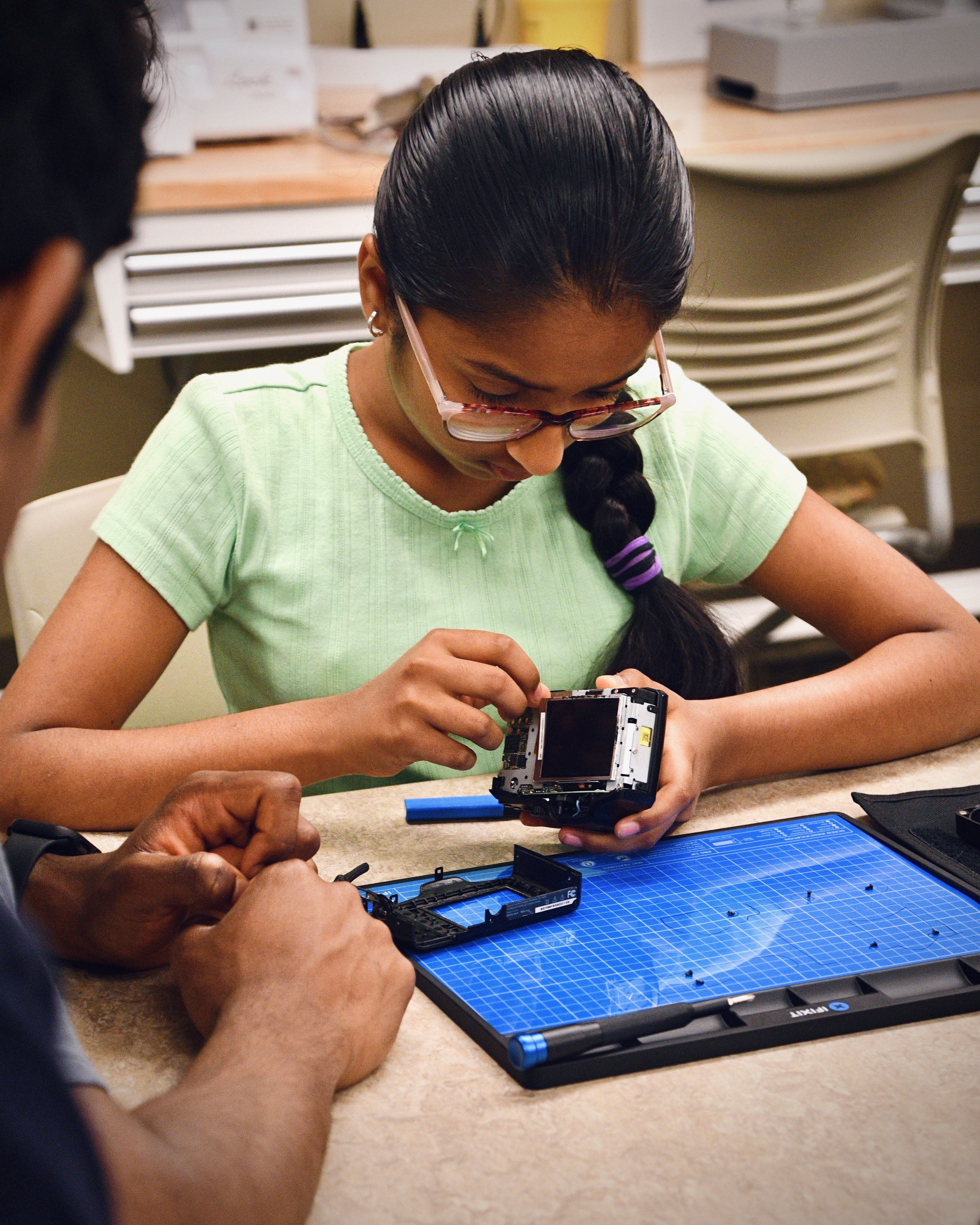 A young student examining a disassembled camera over an iFixit mat