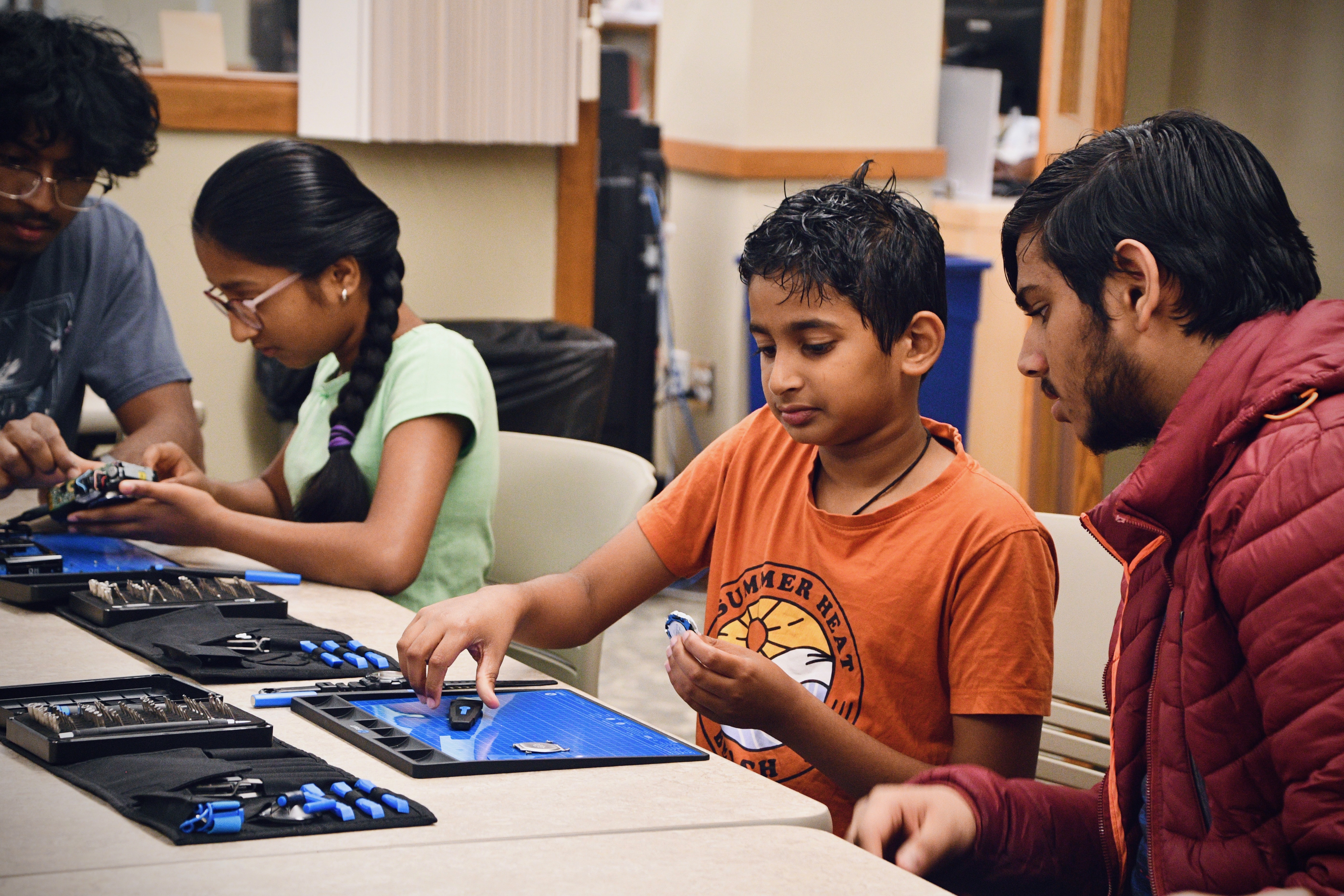 Kids at a workshop table with iFixit toolkits