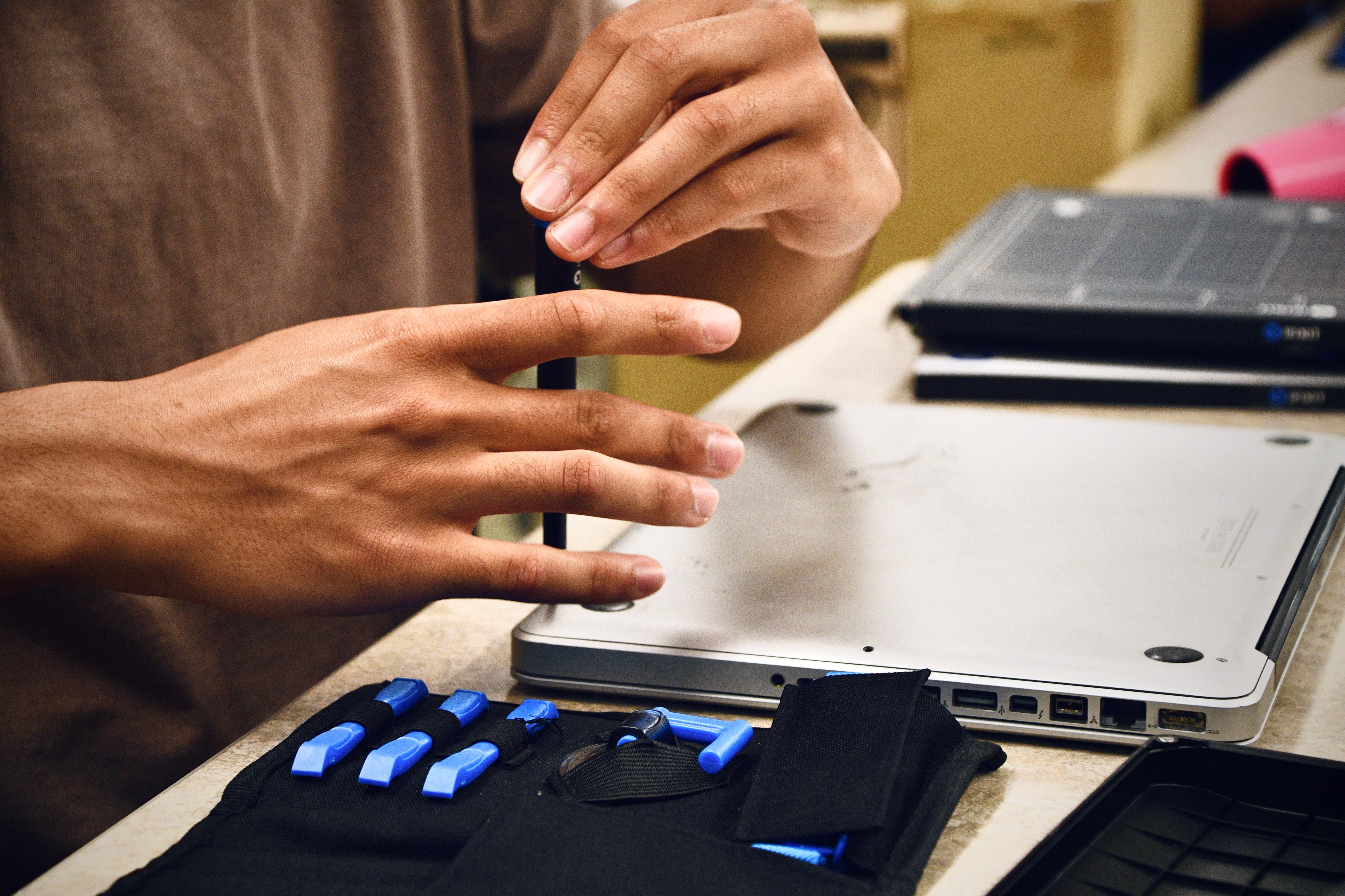 Hands positioning a precision driver over an open MacBook