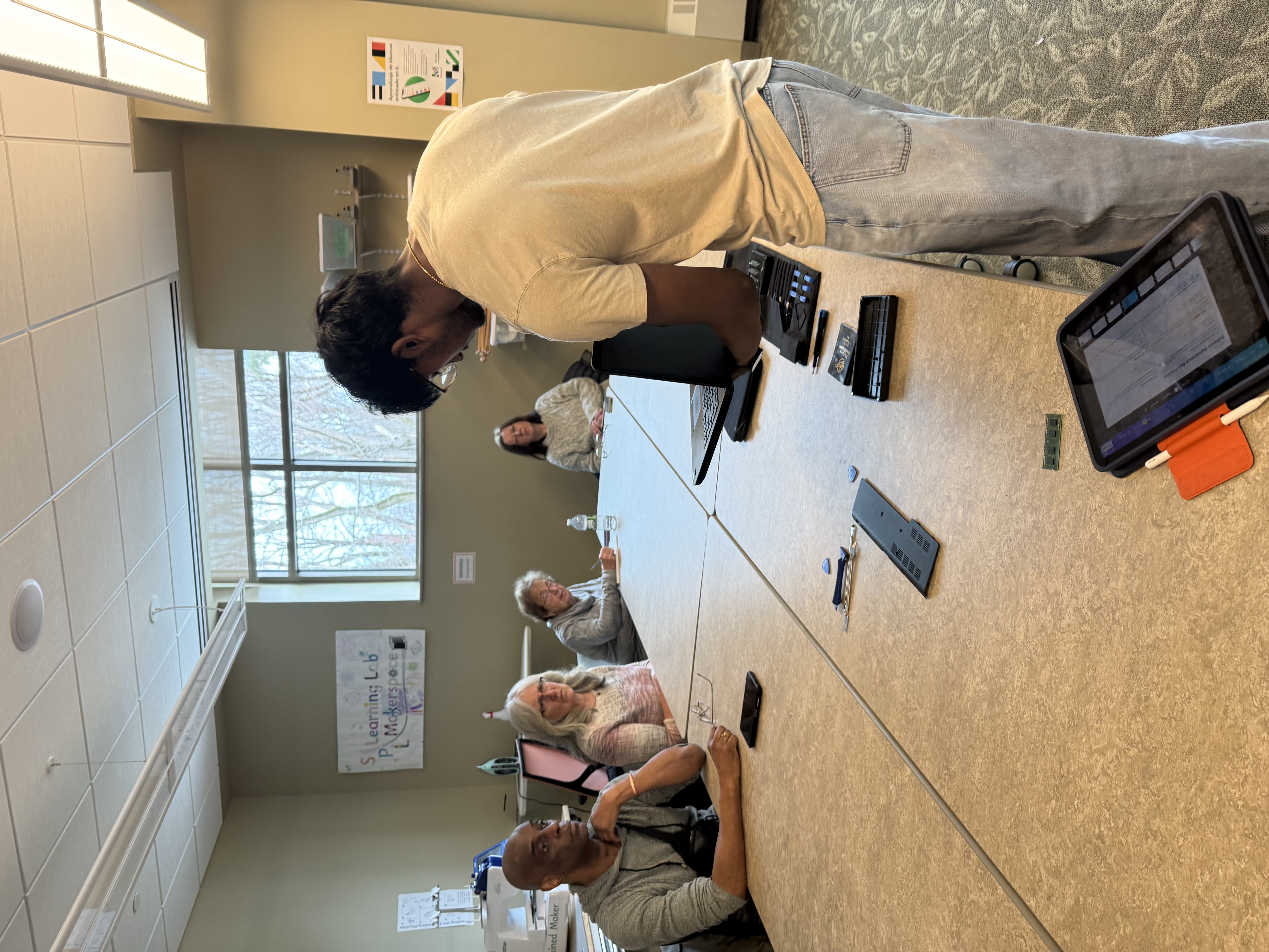 A TAA volunteer teaching a laptop repair to a group seated around a table